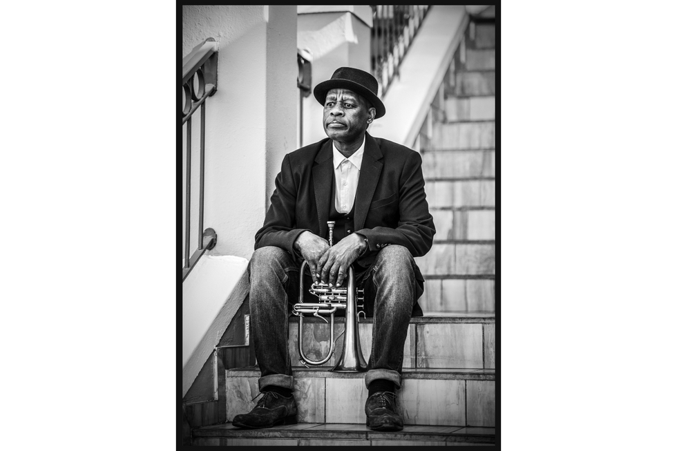 A photograph of South African trumpeter Feya Faku sitting on stairs, holding his trumpet.